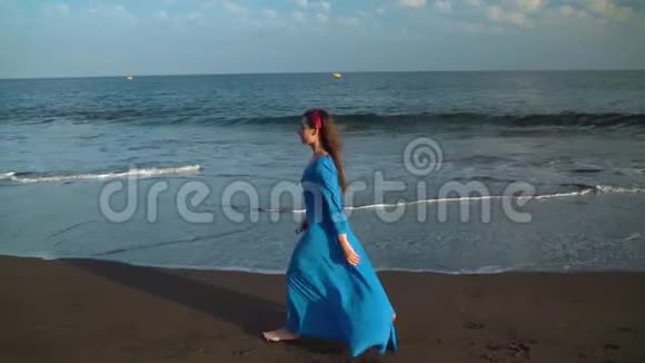穿着漂亮蓝色裙子的女人走在黑色的火山海滩上视频的预览图