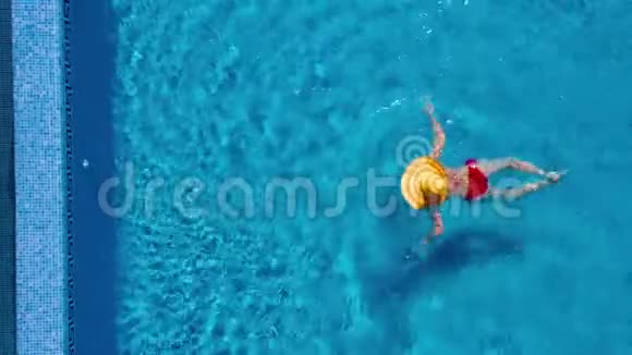 从顶部看一个穿着红色泳衣和一顶黄色大帽子的女人在游泳池里游泳视频的预览图
