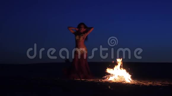 晚上一个在沙滩上跳舞的女孩在明亮的篝火旁跳肚皮舞视频的预览图