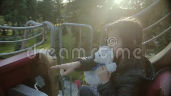 一个快乐的女孩在一个铁路旋转木马与泰迪熊她用手指指着视频的预览图