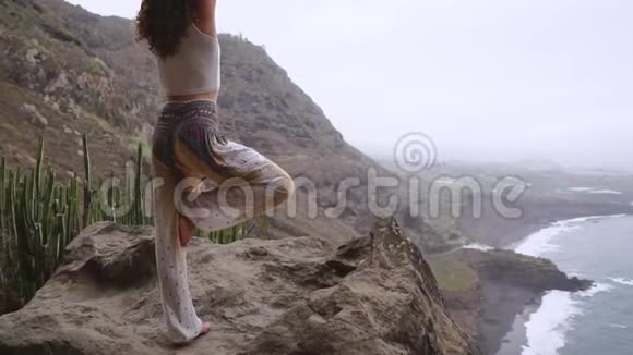 女人冥想瑜伽战士在海洋海滩和岩石山的姿势激励和鼓舞人心的健康和视频的预览图