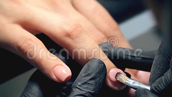 专业的指甲护理过程中化妆师在黑色手套做指甲女性客户的指甲用聚胶盖视频的预览图