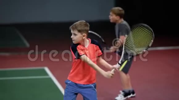 两个快乐的男孩在球场上用球拍发球和回球打网球的儿童正手击球视频的预览图