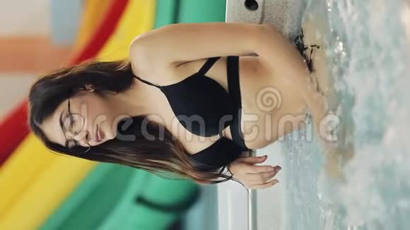 垂直视频戴眼镜的年轻女人在按摩浴缸里放松在相机前摆姿势一个女孩的肖像视频的预览图