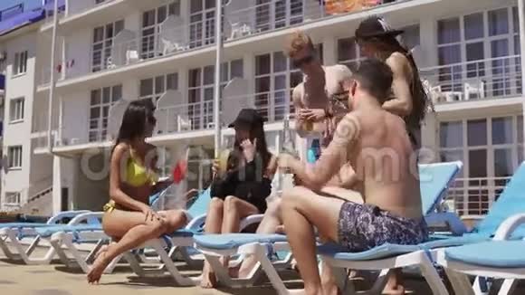 一群漂亮的年轻朋友穿着泳衣喝着鸡尾酒在游泳池旁聊天玩得开心视频的预览图