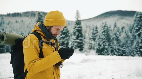 有胡子的人穿着黄色的冬天衣服用手机一个徒步旅行者带着背包去冬山视频的预览图