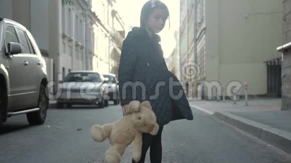 孤独的小女孩带着她的玩具熊在街上摆姿势转身走开了视频的预览图