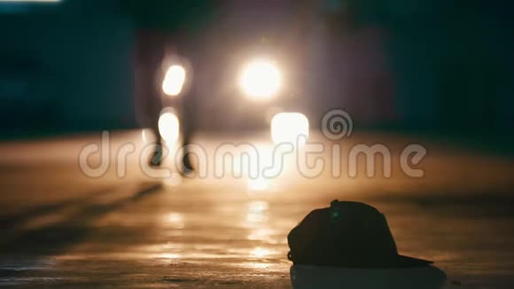 男性在车库行走的剪影在前灯前举起帽子双脚并拢视频的预览图