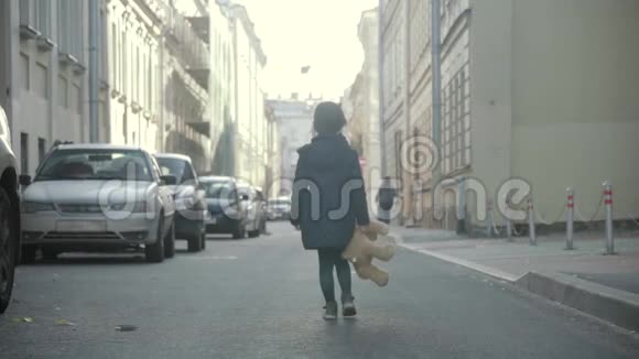 秋天小女孩带着她的泰迪熊沿着一条城市的小巷在斯洛文尼亚视频的预览图