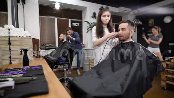两个朋友参观现代理发店帅哥坐在镜子前和发型师合作微笑视频的预览图