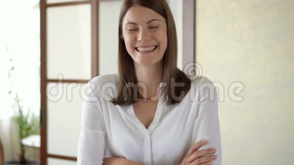 慢动作肖像穿白色上衣的年轻女子站在客厅微笑的手臂交叉视频的预览图