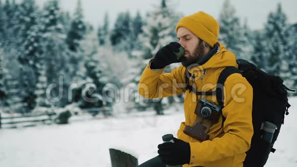 冬天美丽的山有胡子的人穿着黄色的冬装在外面喝热茶或咖啡视频的预览图