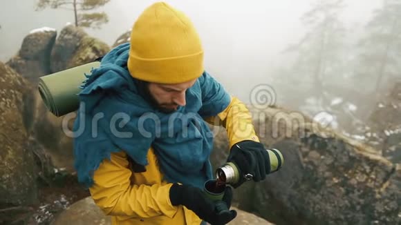 冬天美丽的山有胡子的人穿着黄色的冬装在外面喝热茶或咖啡视频的预览图