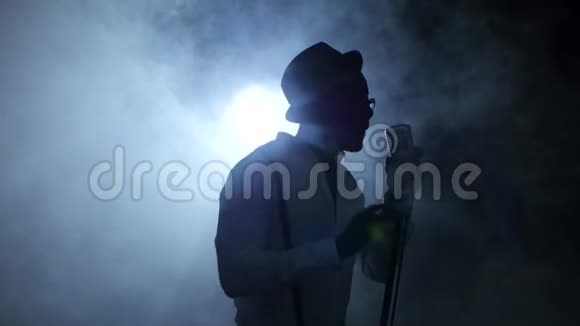 美国黑人男音乐家在烟雾和白光中在录音室唱歌黑色背景剪影视频的预览图
