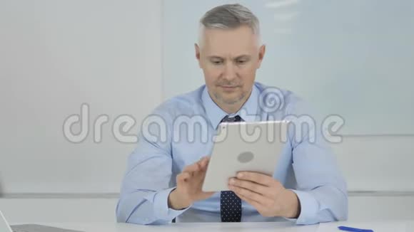 高级商人在办公室平板电脑上浏览互联网视频的预览图