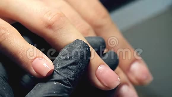 专业的指甲护理过程中化妆师在黑色手套做指甲女性客户的指甲用聚胶盖视频的预览图