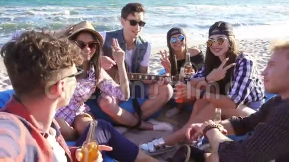 年轻人录制视频或自拍一群朋友坐在沙滩上的安乐椅上弹吉他和视频的预览图