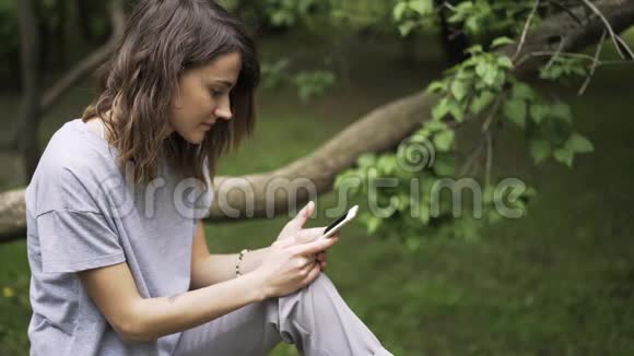 公园里一个带智能手机的年轻女子的侧景视频的预览图