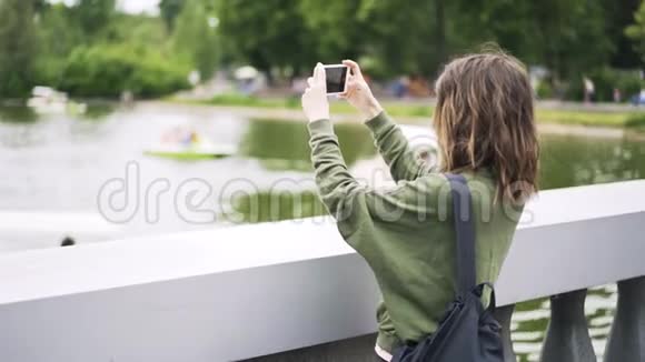 年轻女子带着智能手机在河边拍视频视频的预览图