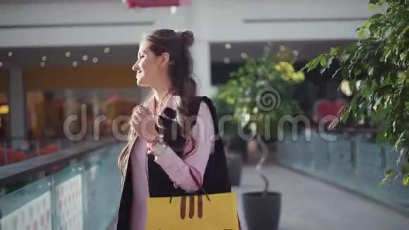 穿着粉红色衬衫的年轻快乐女人正在购物中心散步迷人的女孩正兴高采烈地盘旋着背着视频的预览图