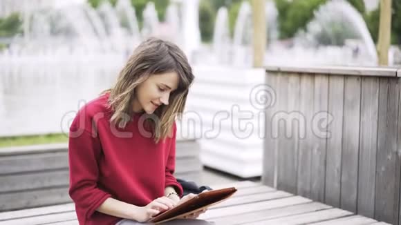 穿红色衣服的年轻女子在喷泉旁用平板电脑工作视频的预览图