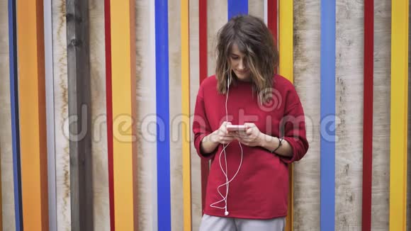 穿红色衣服的年轻女子在五颜六色的墙边发短信和听音乐视频的预览图