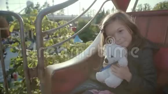 小可爱的女孩抱着她的泰迪熊而她骑着旋转木马视频的预览图