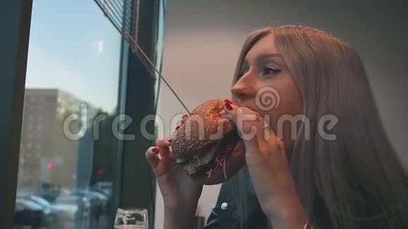 一个女孩特写的肖像手里拿着一个汉堡包一个年轻漂亮的女人在咖啡馆吃汉堡包食品快餐视频的预览图