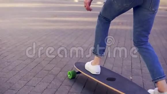 女穿着蓝色牛仔裤和白色运动鞋开始在鹅卵石铺成的长板上玩滑板的特写镜头视频的预览图