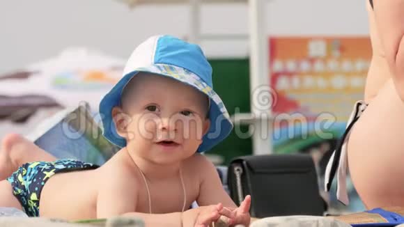 可爱的小宝宝戴着一顶大帽子坐在海滩上微笑视频的预览图