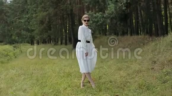 穿着白色衣服的年轻女子摆姿势戴着黑色眼镜走在草地上视频的预览图