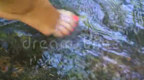 赤足的女孩在一条水流湍急的河流中她的脚在水中溅起粉红色的踏板视频的预览图
