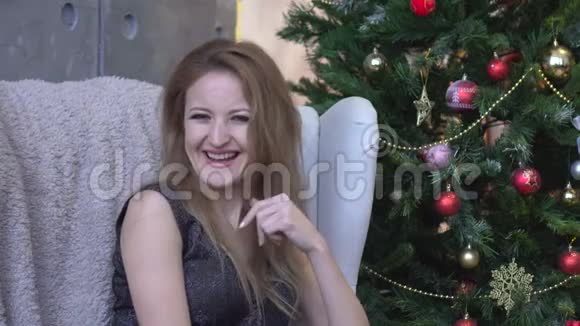 年轻迷人的快乐女人笑着坐在圣诞树的背景上视频的预览图