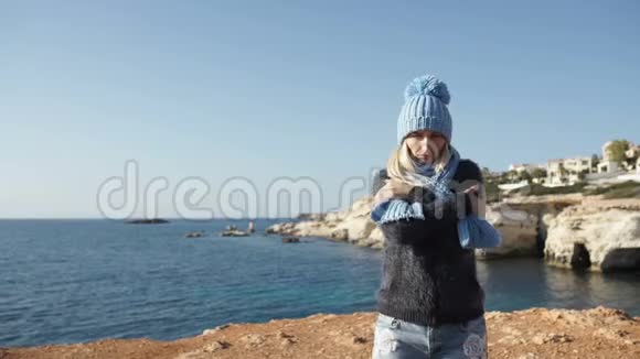 蓝色海洋背景下穿着温暖衣服的年轻女子视频的预览图