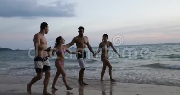 日落时分一群朋友在海滩散步两对游客牵着手在海边聊天视频的预览图