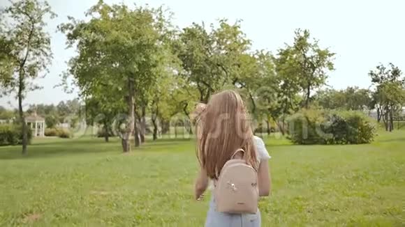一个年轻的女学生背着一个背包手里拿着笔记正在公园里散步在学习期间休息视频的预览图