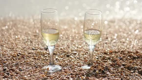 两杯香槟站在沙滩上海边有小贝壳背景中海浪冲刷着海岸视频的预览图