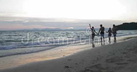 人们在夕阳下的沙滩上散步快乐的男男女女晚上在海边聊天两对情侣牵手视频的预览图