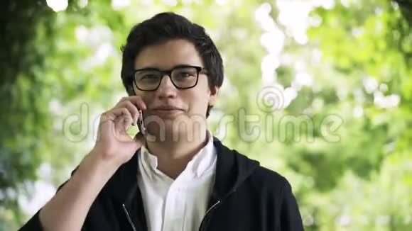 戴眼镜的年轻人正在打电话在公园里散步视频的预览图
