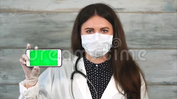 身穿白大褂戴着防护面具的女医护人员手持智能手机视频的预览图