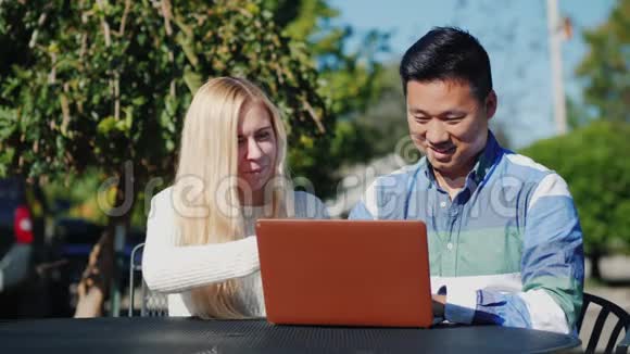 年轻的白种人女人和中国男人一起使用笔记本电脑在户外咖啡馆休息一下视频的预览图