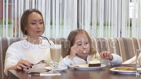 美丽的年轻妈妈和小女儿一起在舒适的咖啡馆里吃蛋糕视频的预览图