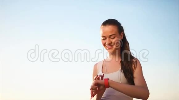 年轻漂亮的微笑女人在外面用她的智能手表装置视频的预览图