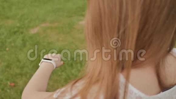 年轻女孩在公园散步时触摸到一个智能时钟的触摸屏积极的生活方式体育运动娱乐视频的预览图