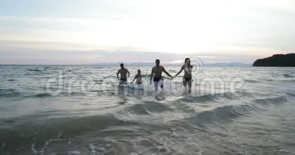 两位从水海手中奔跑的情侣在夕阳下的沙滩上组成了年轻的朋友小组他们拥有欢乐的混合种族和视频的预览图