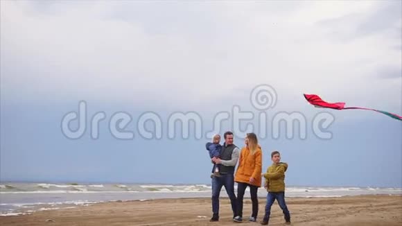 一个年轻的家庭在寒冷的天气里带着风筝沿着海滩散步视频的预览图