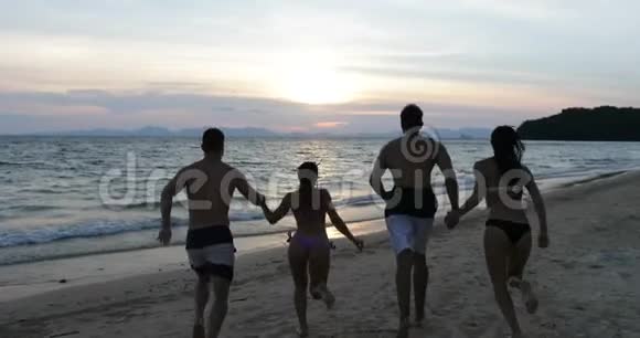 一群在海上奔跑的人手挽手背着欢乐的朋友一起在夕阳下的沙滩上嬉戏视频的预览图