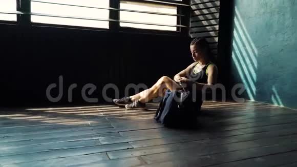 惊慌失措的年轻美女坐在地板上用黑色拳击包裹在俱乐部里的手视频的预览图