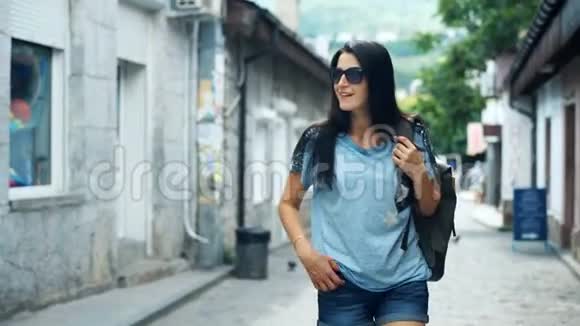 快乐的女游客肩上背着背包走在老式建筑附近的街道上视频的预览图