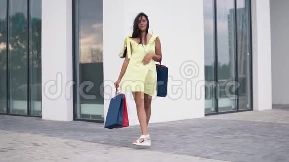 漂亮的女孩模特穿着一件长裙手里拿着彩色袋子购物后慢动作视频的预览图